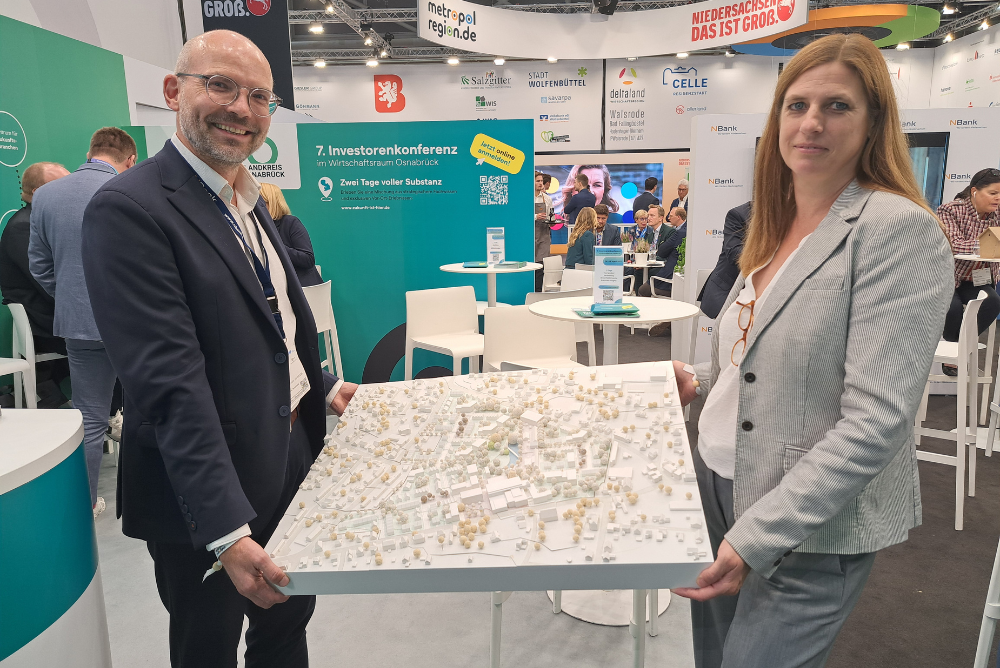 Werbefoto auf der Expo Real zeigt Geschäftsführerin und Geschäftsführer mit Modell des Homann Geländes der OLEG